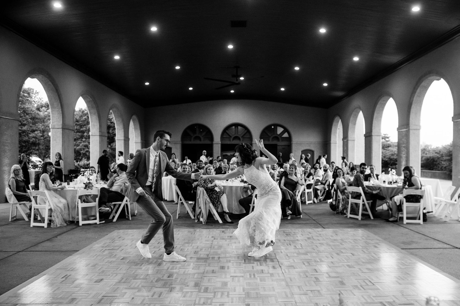 Black and white photo of a couple dancing during their wedding reception in an elegant columned hall.