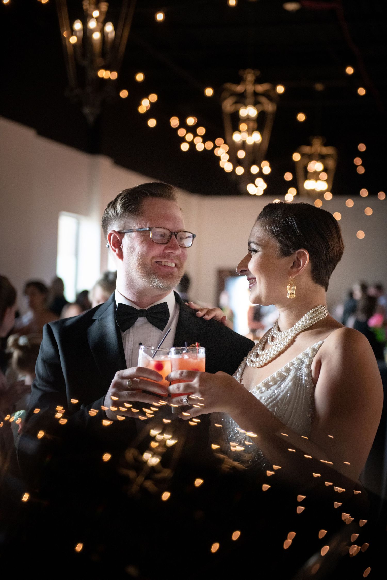 Couple sharing drinks under romantic lighting at their wedding reception.