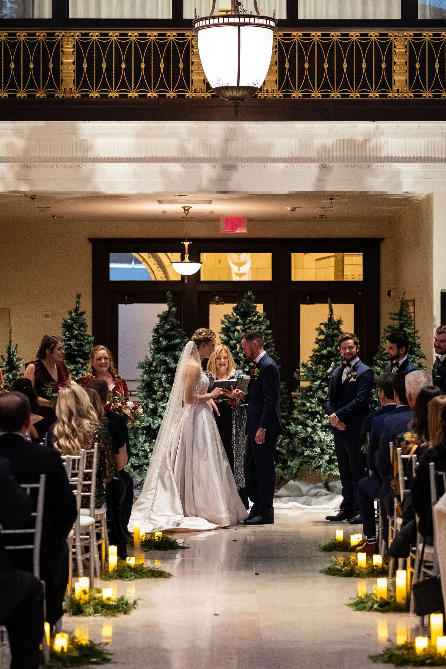 Wedding ceremony with candlelit aisle and Christmas trees under ornate architectural details.