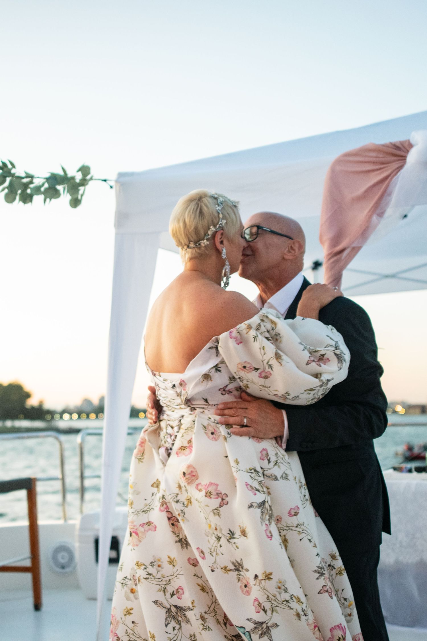 Romantic kiss between newlyweds during sunset waterfront reception.