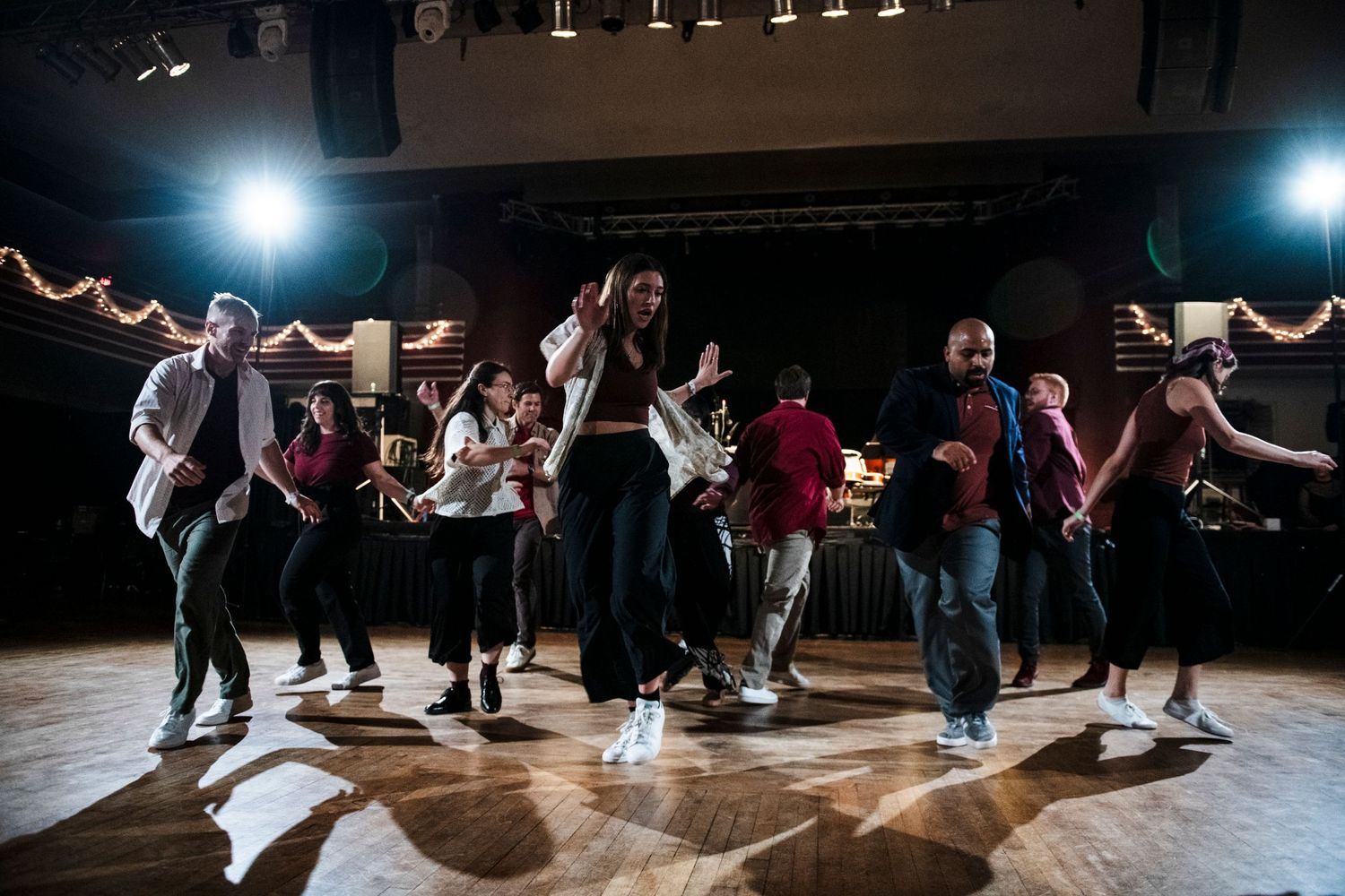 Dancers execute dynamic swing dance moves in formation on an illuminated dance floor.