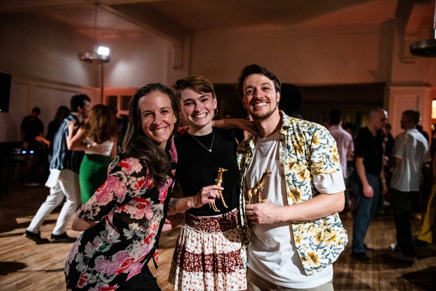Three dancers pose together at swing dance social event with festive lighting.