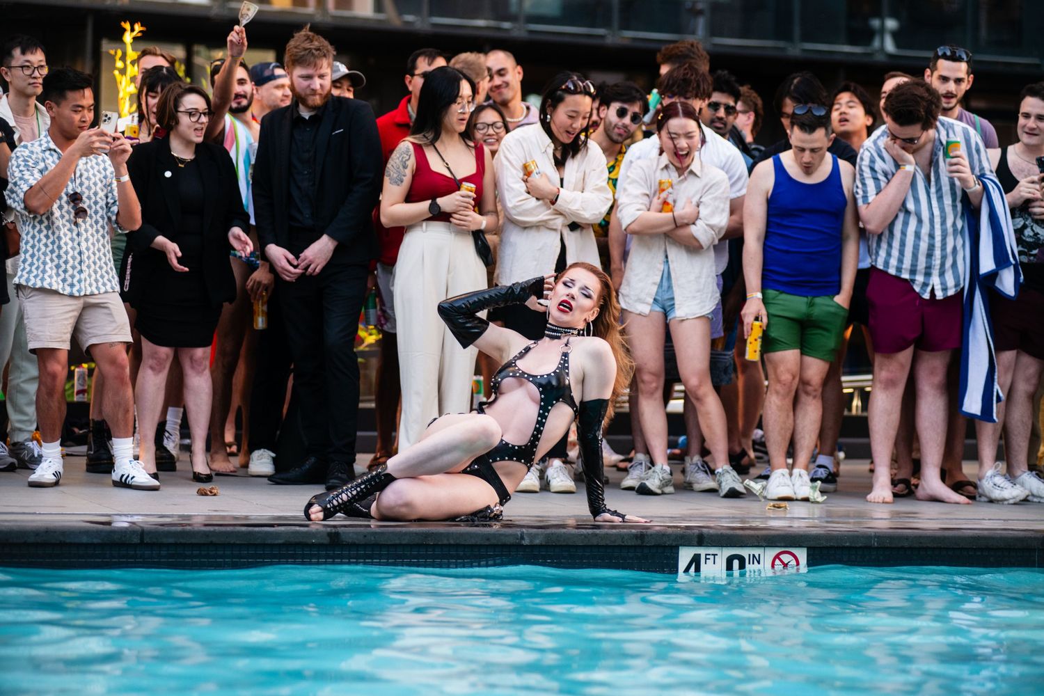 Party guests gather around the pool edge to watch performers at an outdoor event.