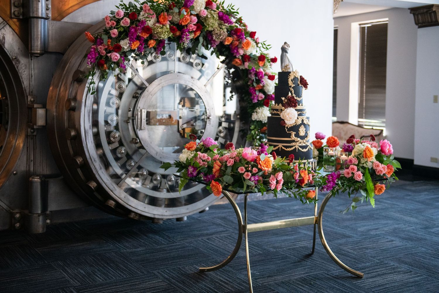 Wedding cake display with circular metal backdrop and colorful floral arch arrangement.