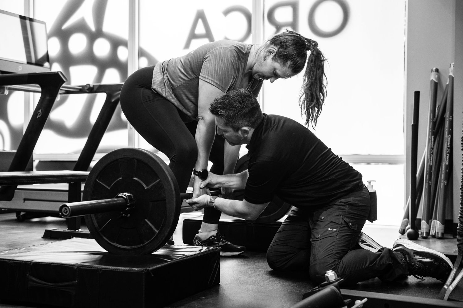 Black and white image of weight training session with barbell in gym setting.