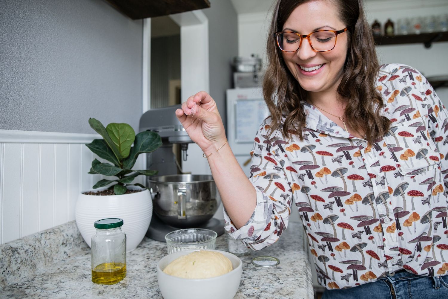 In a kitchen, someone wearing a patterned shirt works at a counter with a stand mixer nearby.