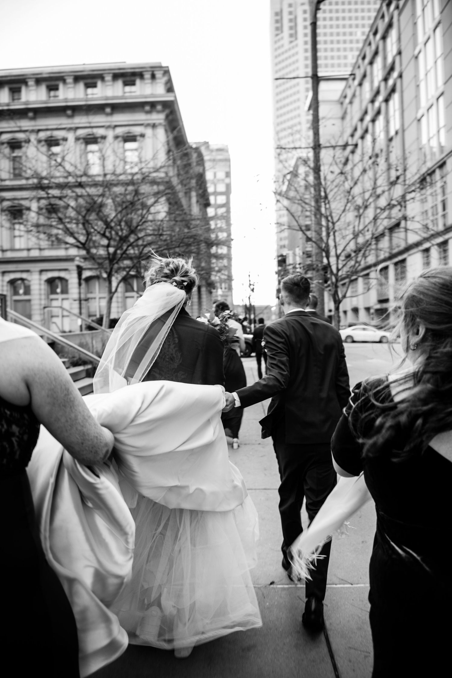 Black and white candid of wedding party walking down city street.