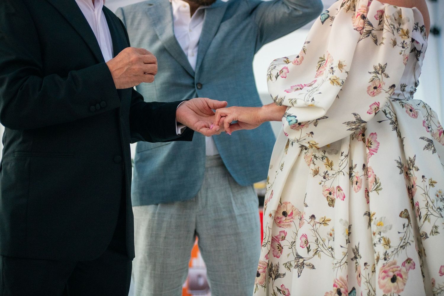 Wedding ceremony detail of ring exchange with floral dress in frame.