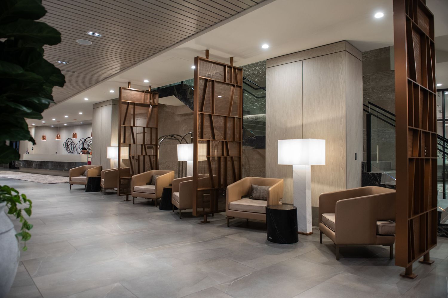 Contemporary lounge area with wooden dividers, tan armchairs, and modern lighting fixtures.