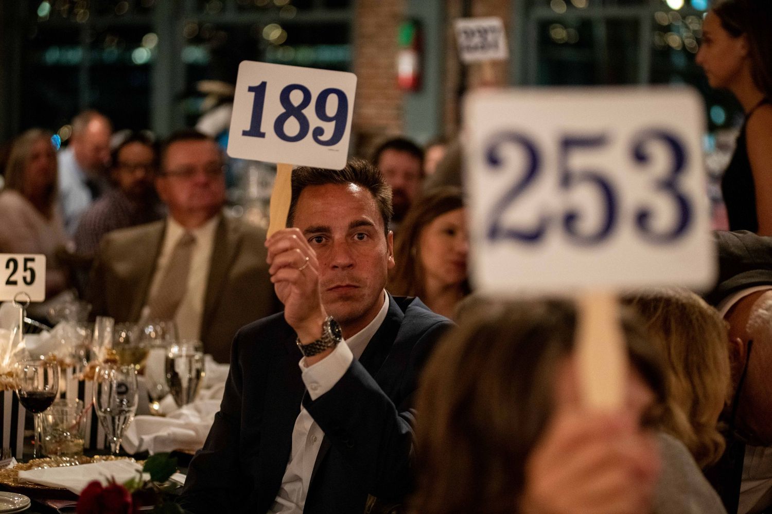 Auction participants holding up numbered bidding paddles during an elegant dinner event.