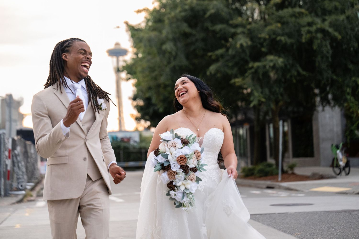 Wedding party members sharing joyful moments outdoors with trees and buildings in background.