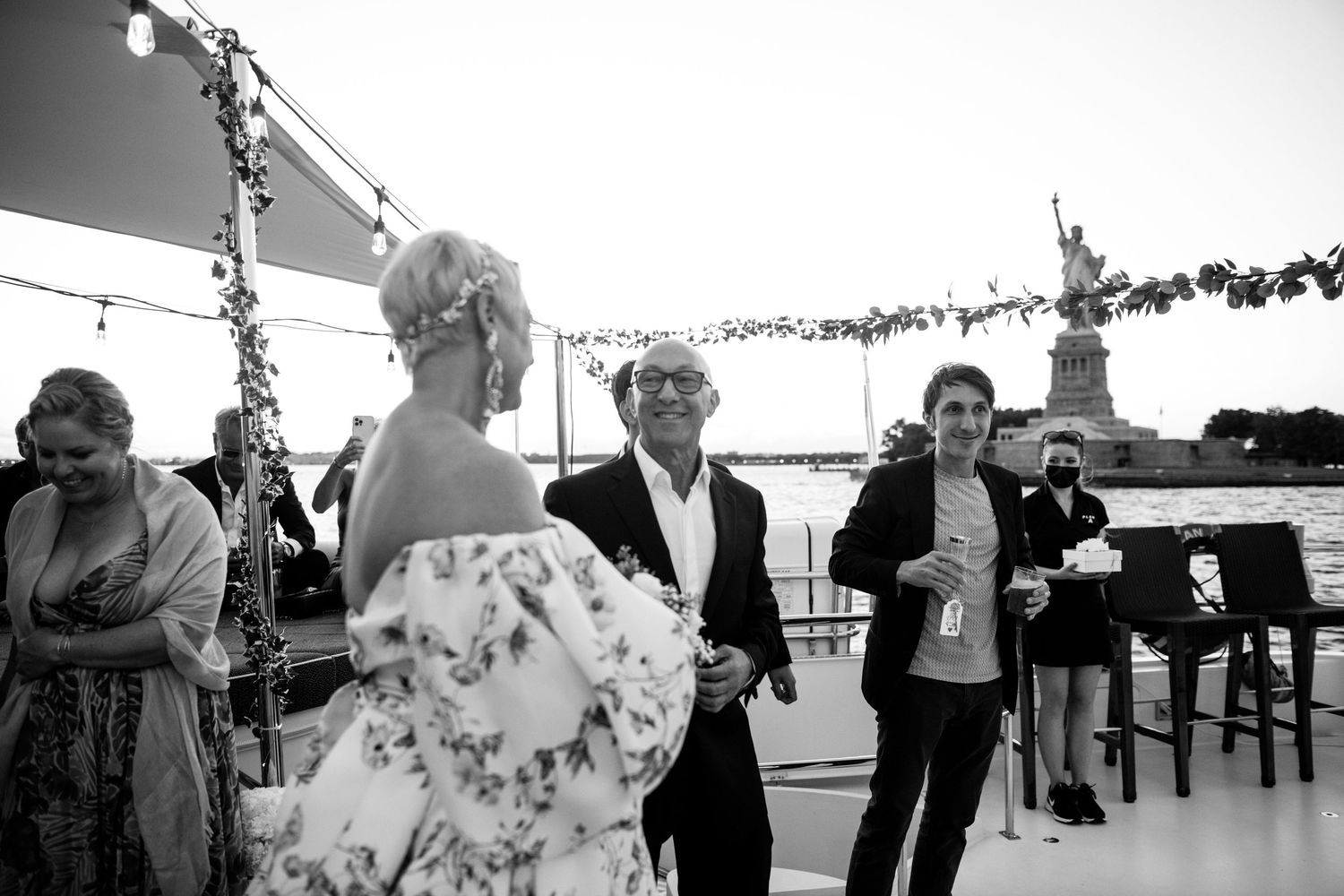 Black and white photo of wedding party celebrating on deck with string lights.