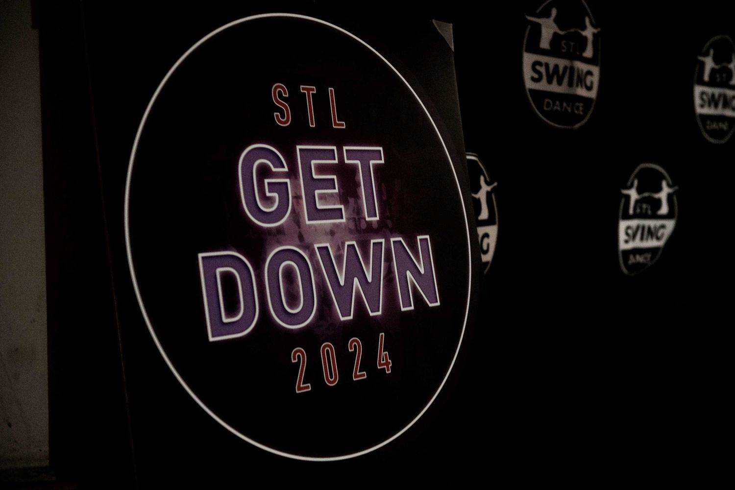 Neon sign reading 'STL GET DOWN 2024' glowing against dark background.
