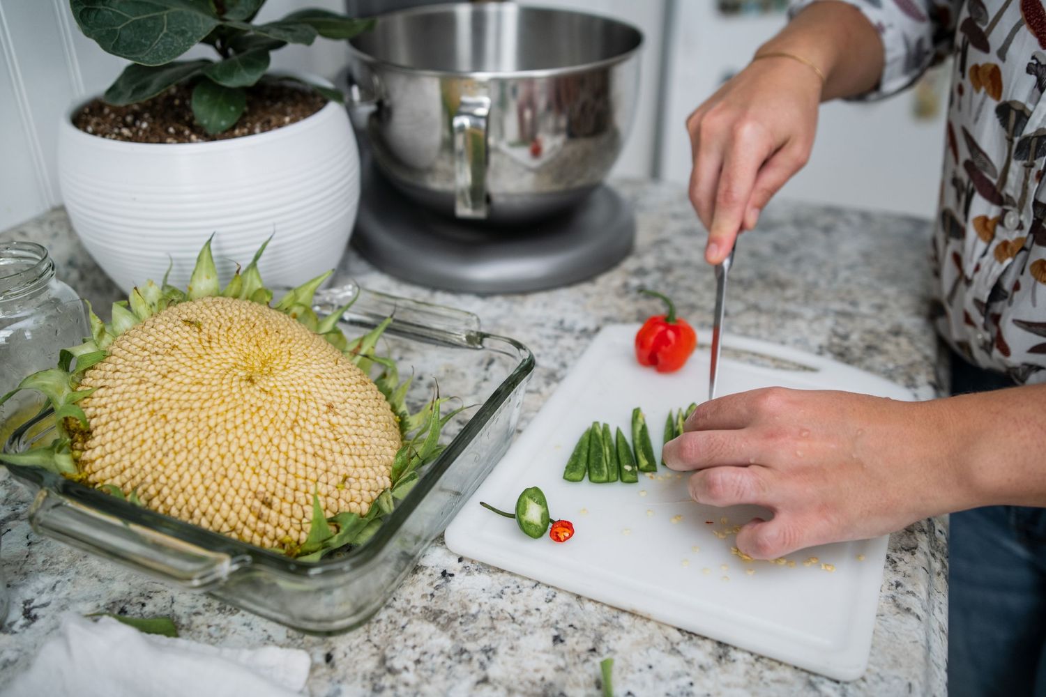 Hands chopping vegetables next to a large yellow melon on a cutting board.