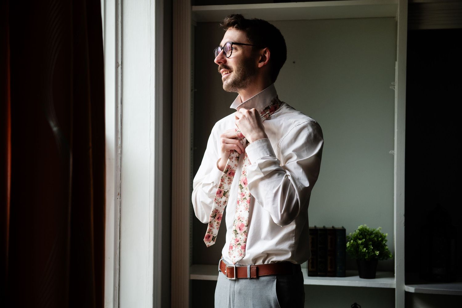 A person adjusting their tie while getting ready by a window in natural light.