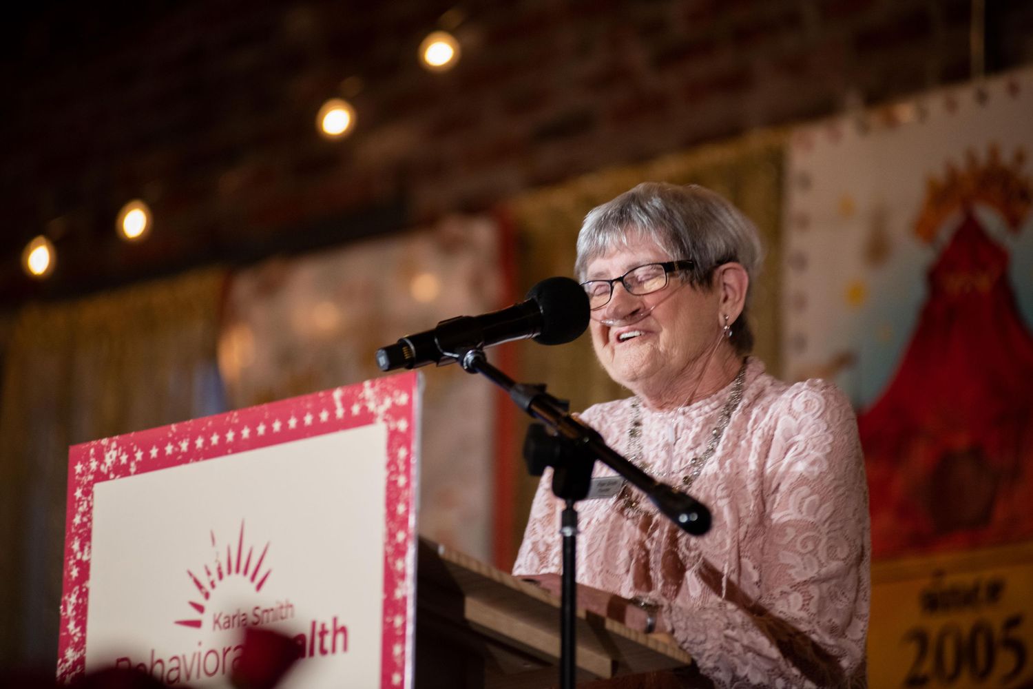 Speaker at podium with pink framed signage and brick wall backdrop during evening event.