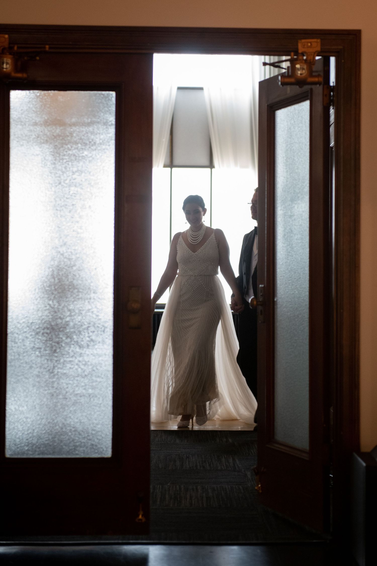 Silhouetted figures in doorway with frosted glass panels creating ethereal wedding moment.