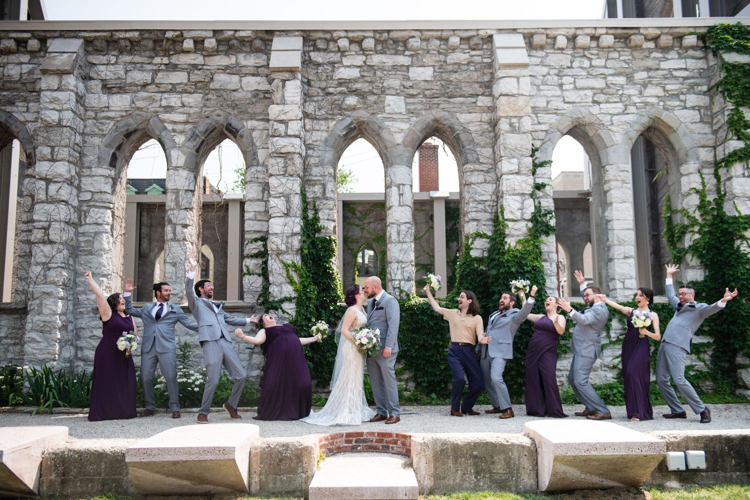 Celebration shot of wedding party jumping in front of historic stone church ruins.
