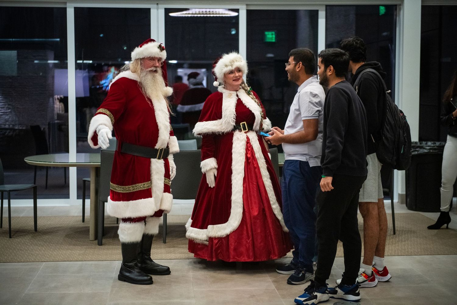 Santa and Mrs. Claus in traditional red velvet costumes interact with guests at an indoor event.