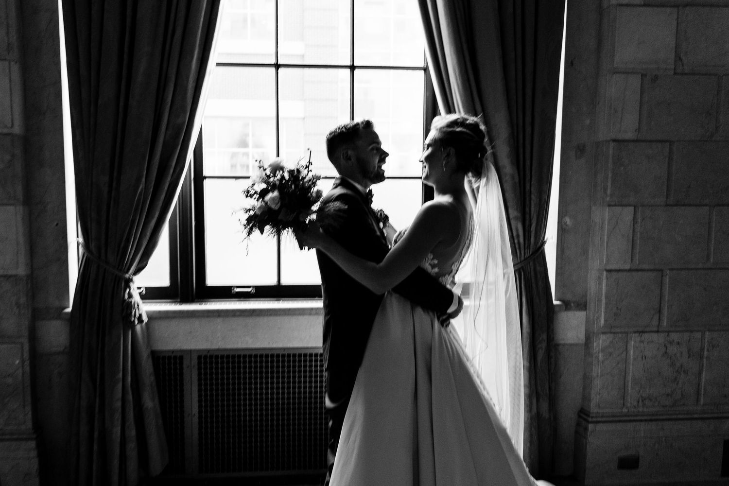 Dancing couple twirling in formal attire by large window with natural light.