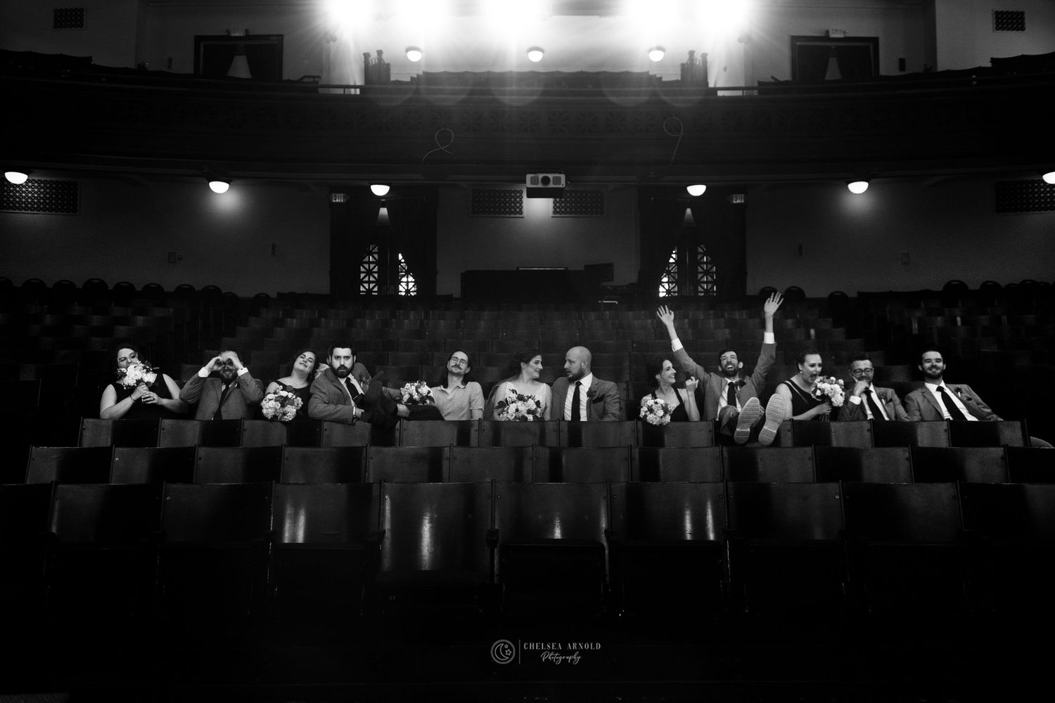 Wedding party lined up in dark theater balcony for dramatic black and white photo.