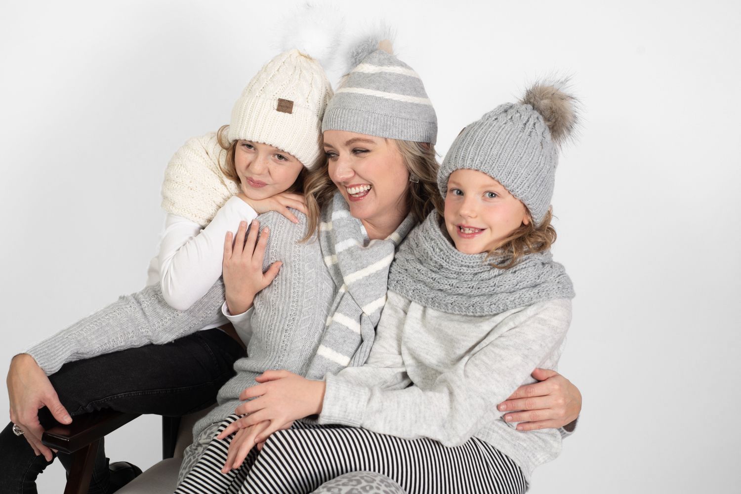 Three people in winter wear sharing warm embraces and smiles against white background.