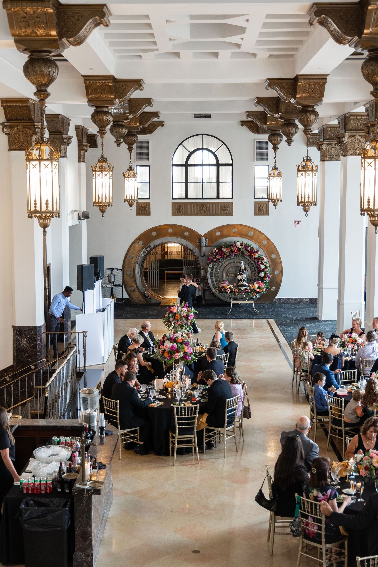 Elegant wedding reception venue with vintage bank vault doors and hanging lanterns in white and gold decor.