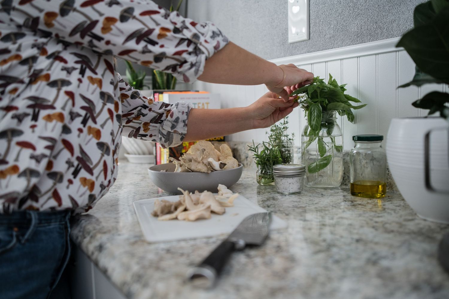 Hands arranging fresh herbs and ingredients on a marble kitchen counter with glass containers.