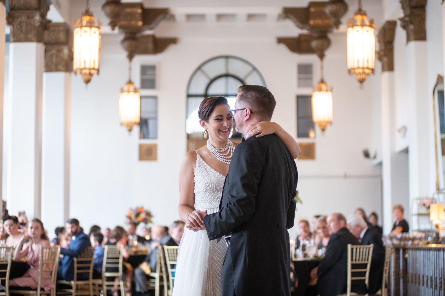 A romantic first dance moment at an elegant wedding reception with ornate lighting and architecture.