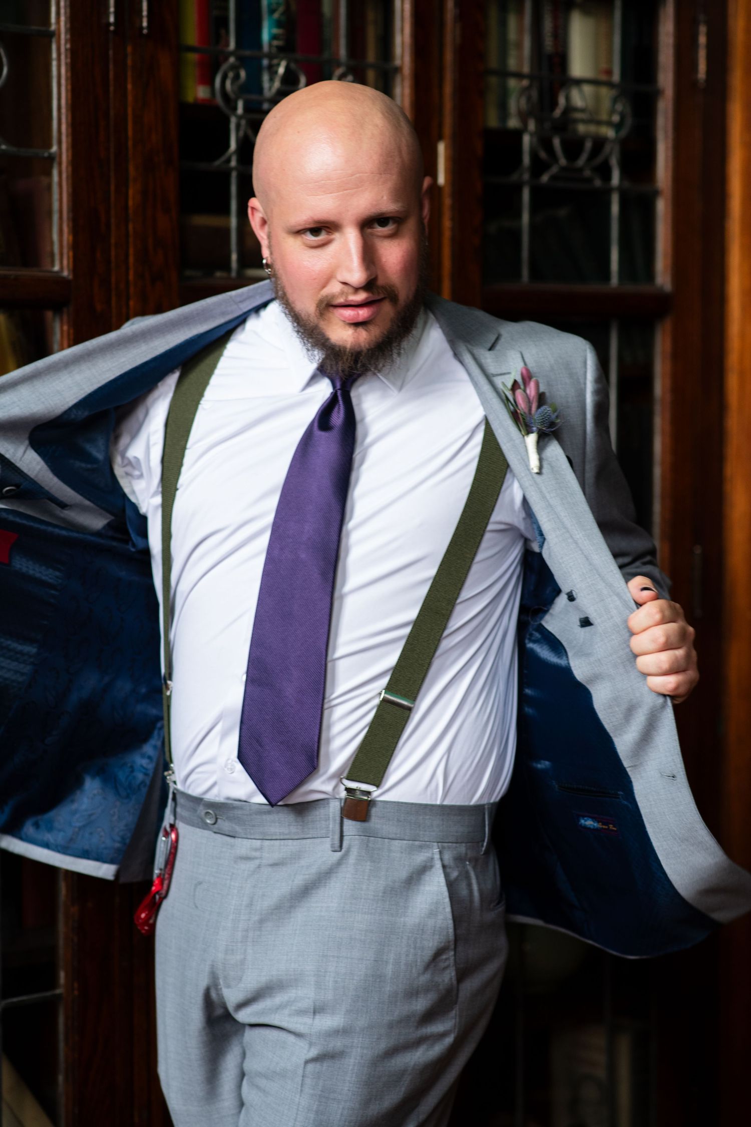 Wedding party member in suspenders and gray suit shows off the lining of his suit jacket.