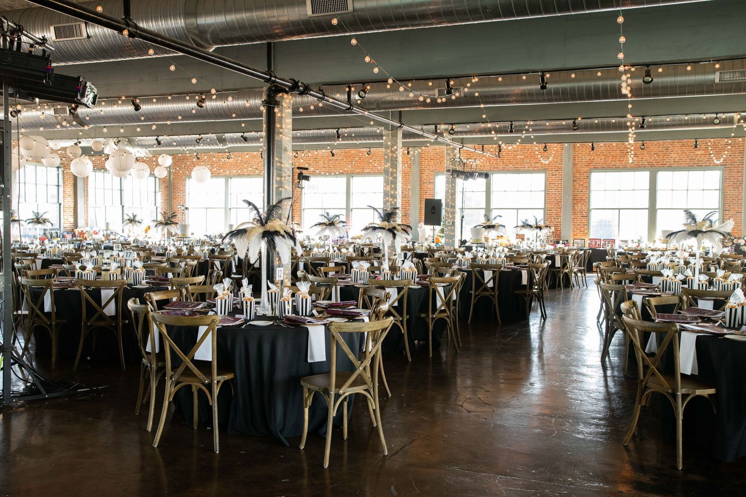 Industrial chic reception venue with cross-back chairs and elegant table settings under exposed ceiling beams.