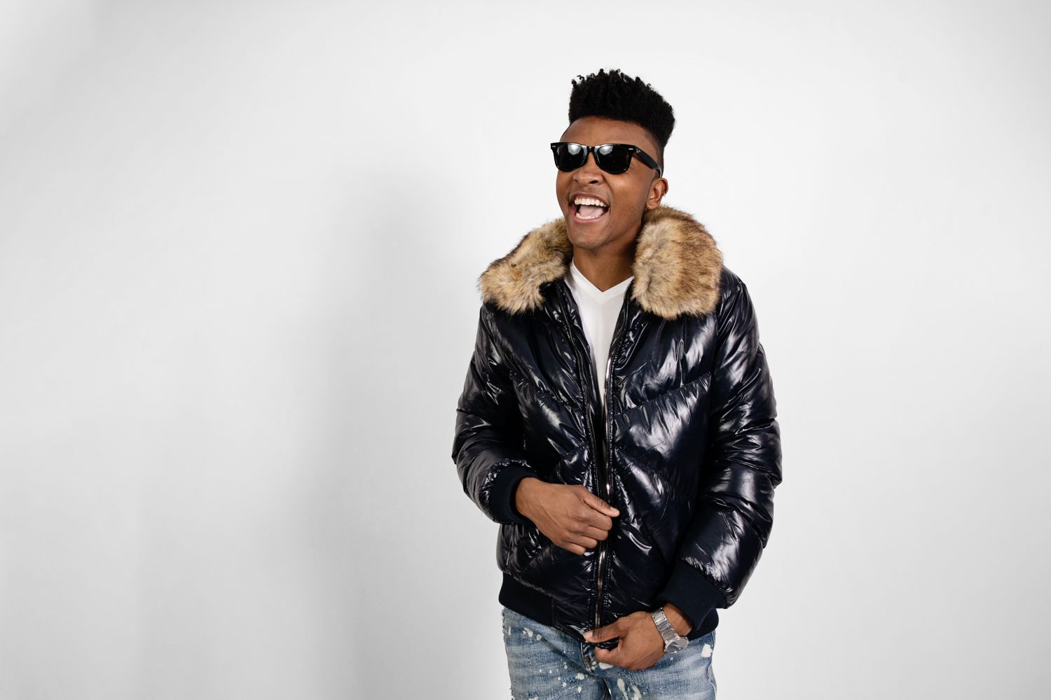 Model wearing sunglasses and black puffer jacket poses with bright expression.