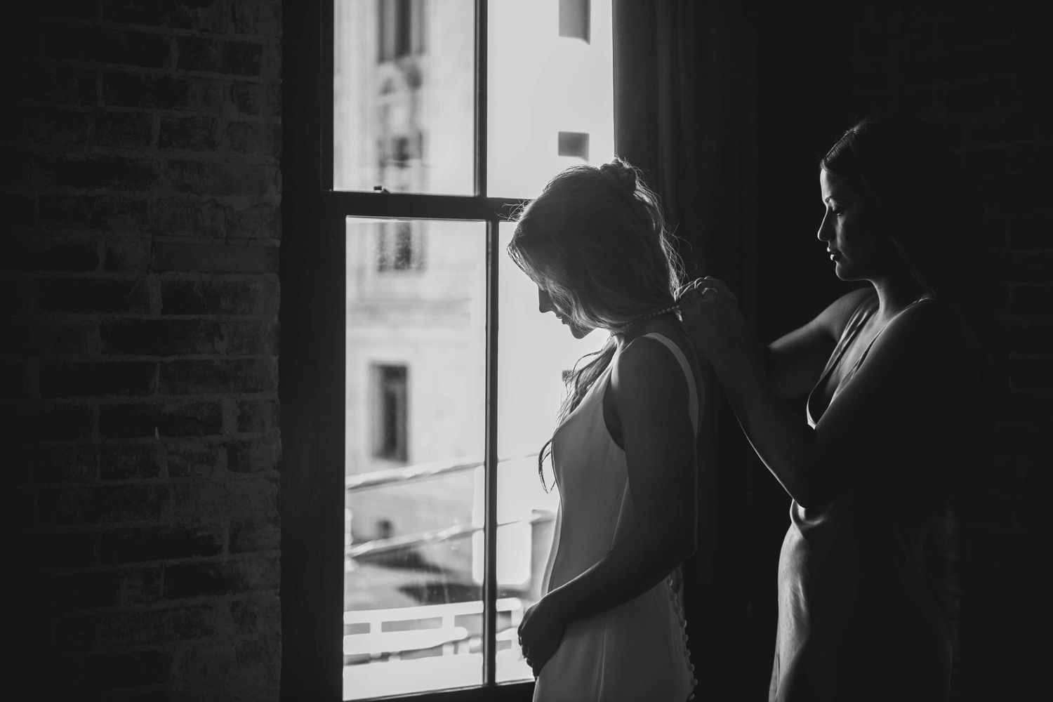 Black and white silhouette of two figures standing by a window in dramatic lighting.