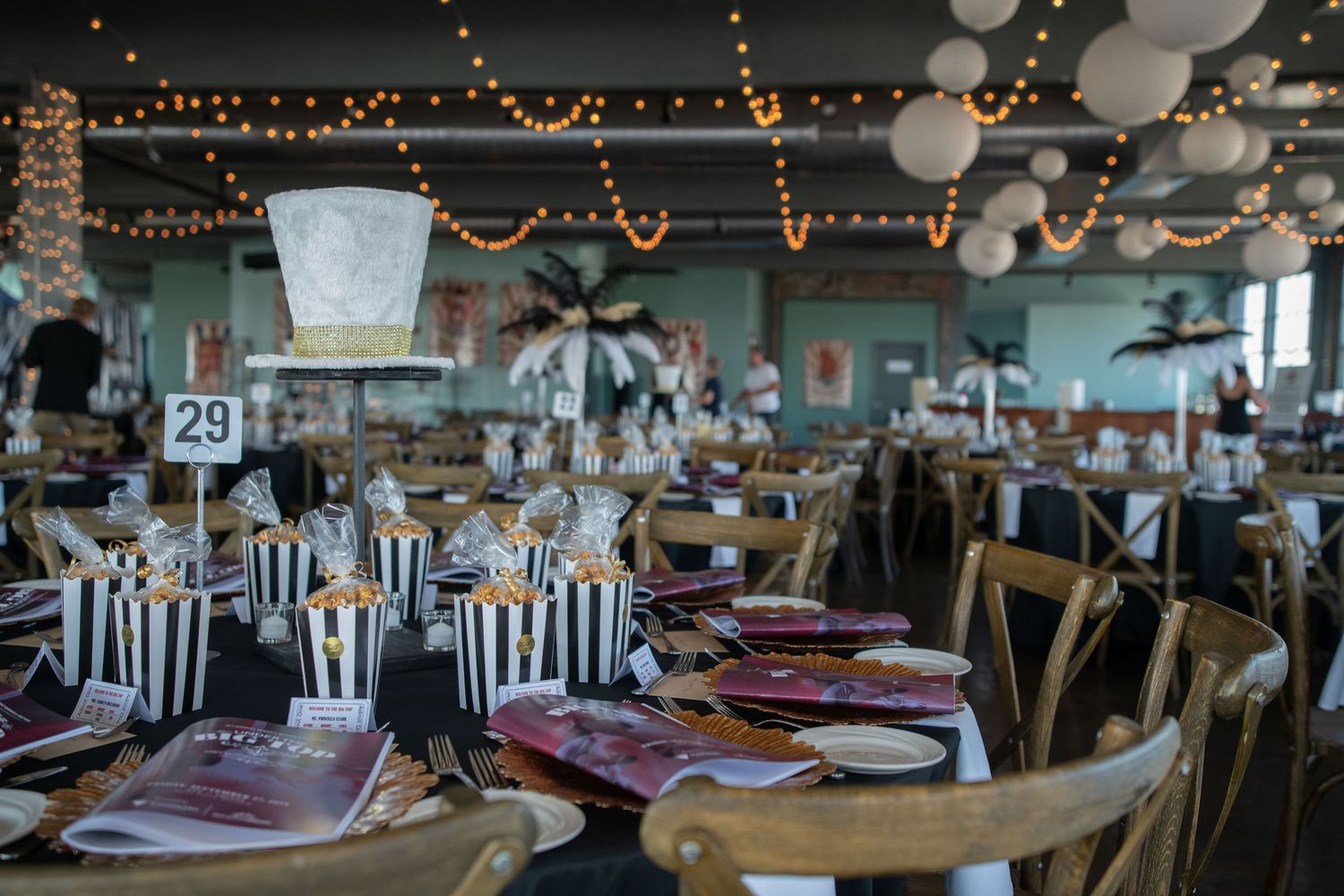 Event space decorated with string lights, white balloons, and black and white striped table settings.