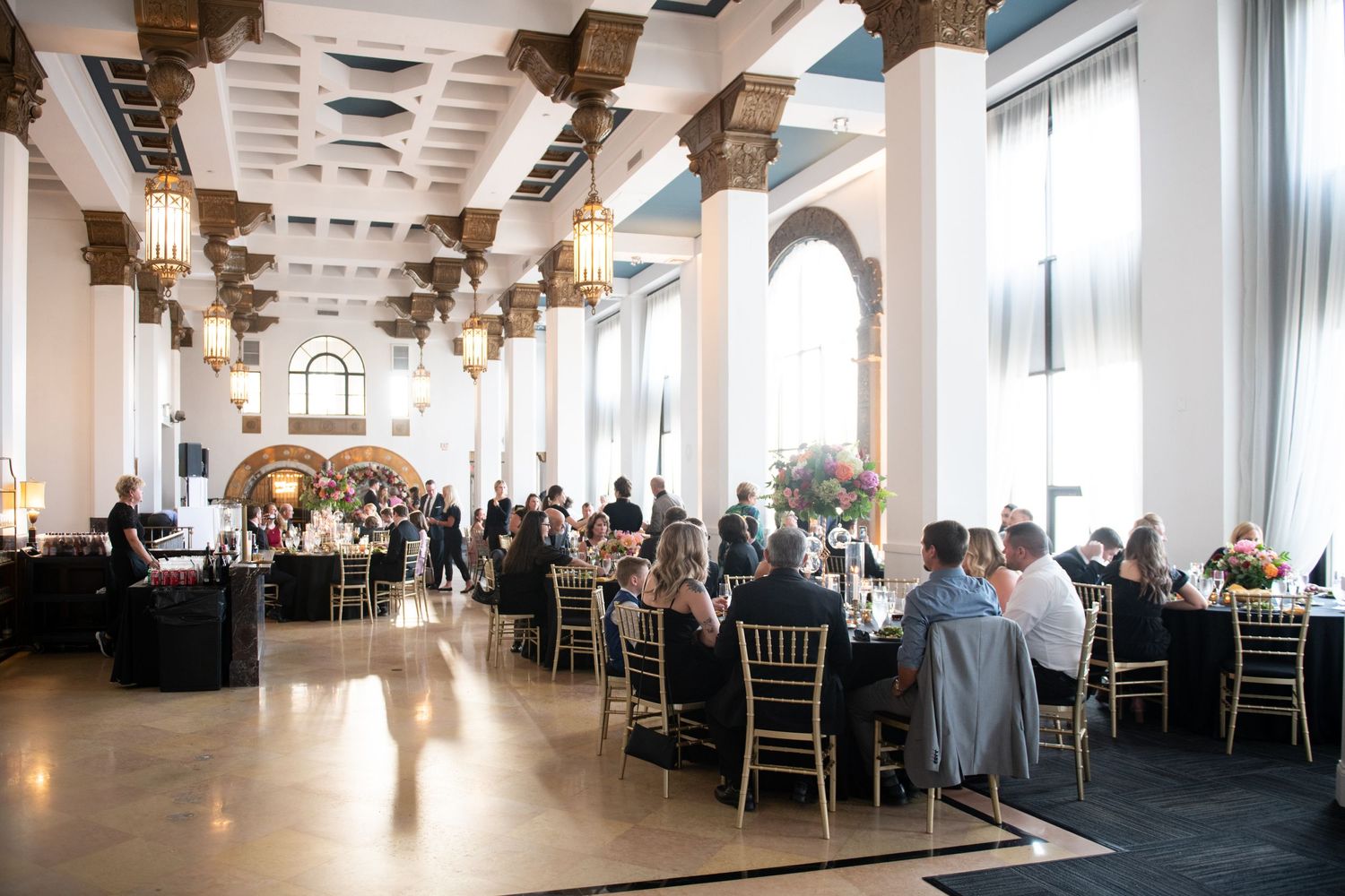 Grand reception hall with ornate columns and ceiling features filled with dining tables and guests.