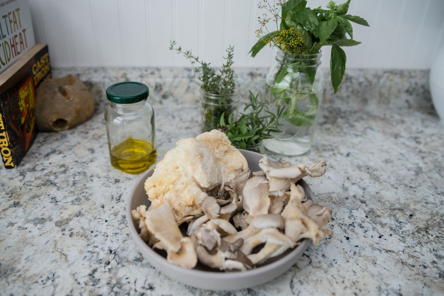 Fresh mushrooms and herbs arranged on a marble countertop with glass containers.