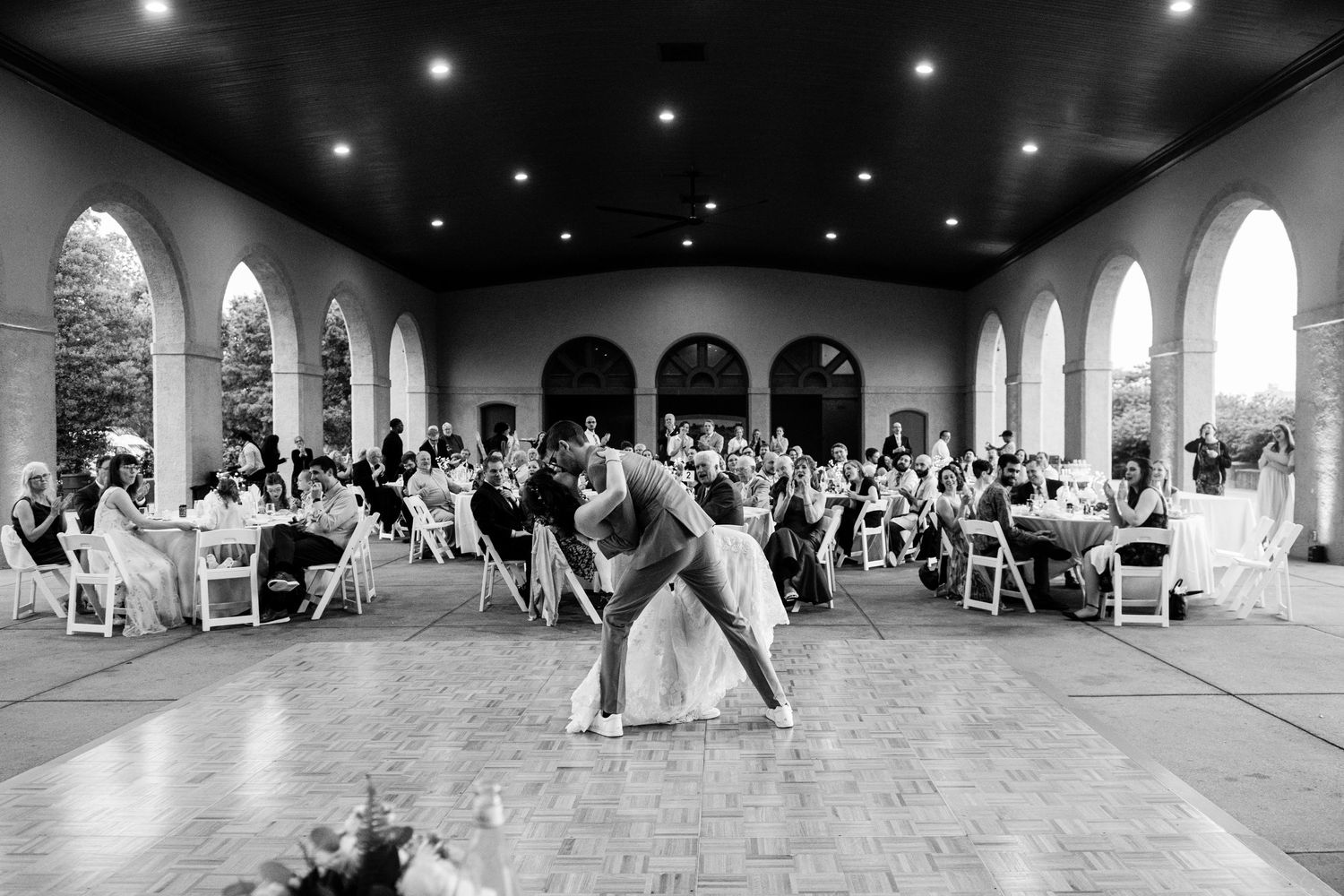 Dramatic black and white photo of a wedding dance dip in front of seated reception guests.