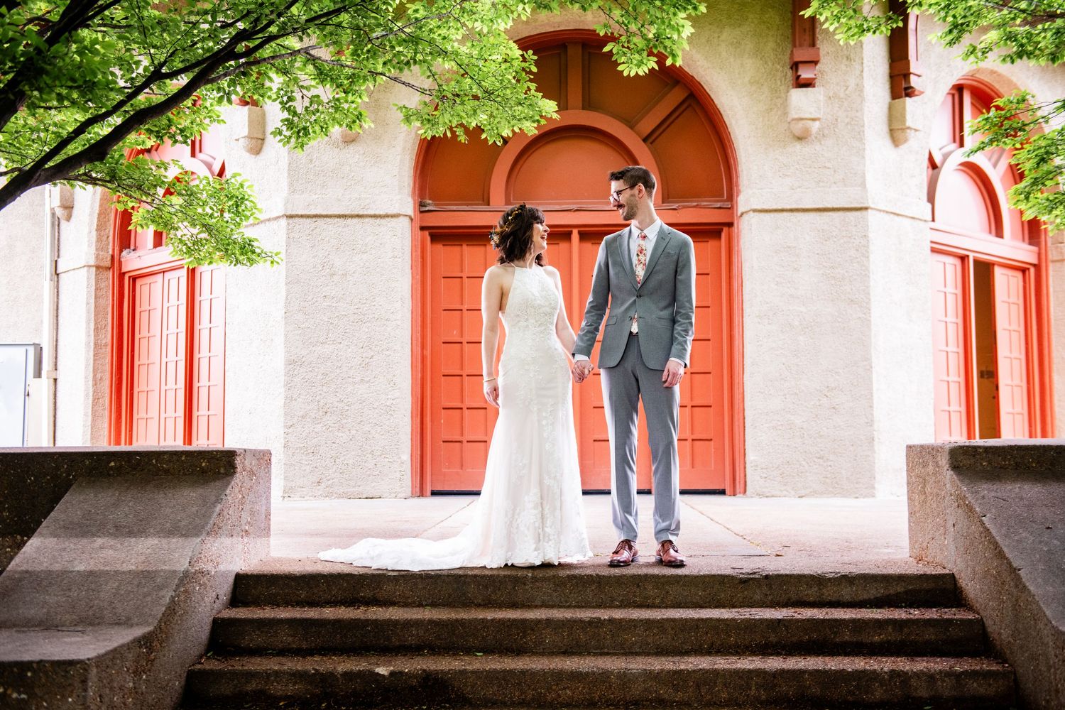 Wedding couple standing on steps in front of orange doorway of historic building.