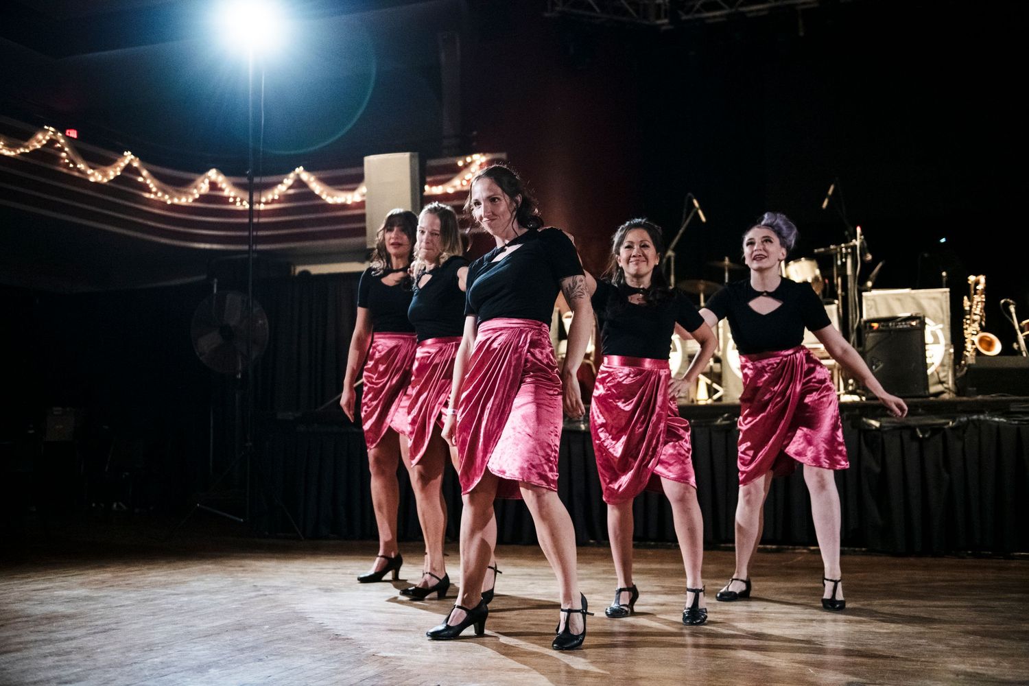 Dancers in pink skirts perform synchronized routine under stage lighting.