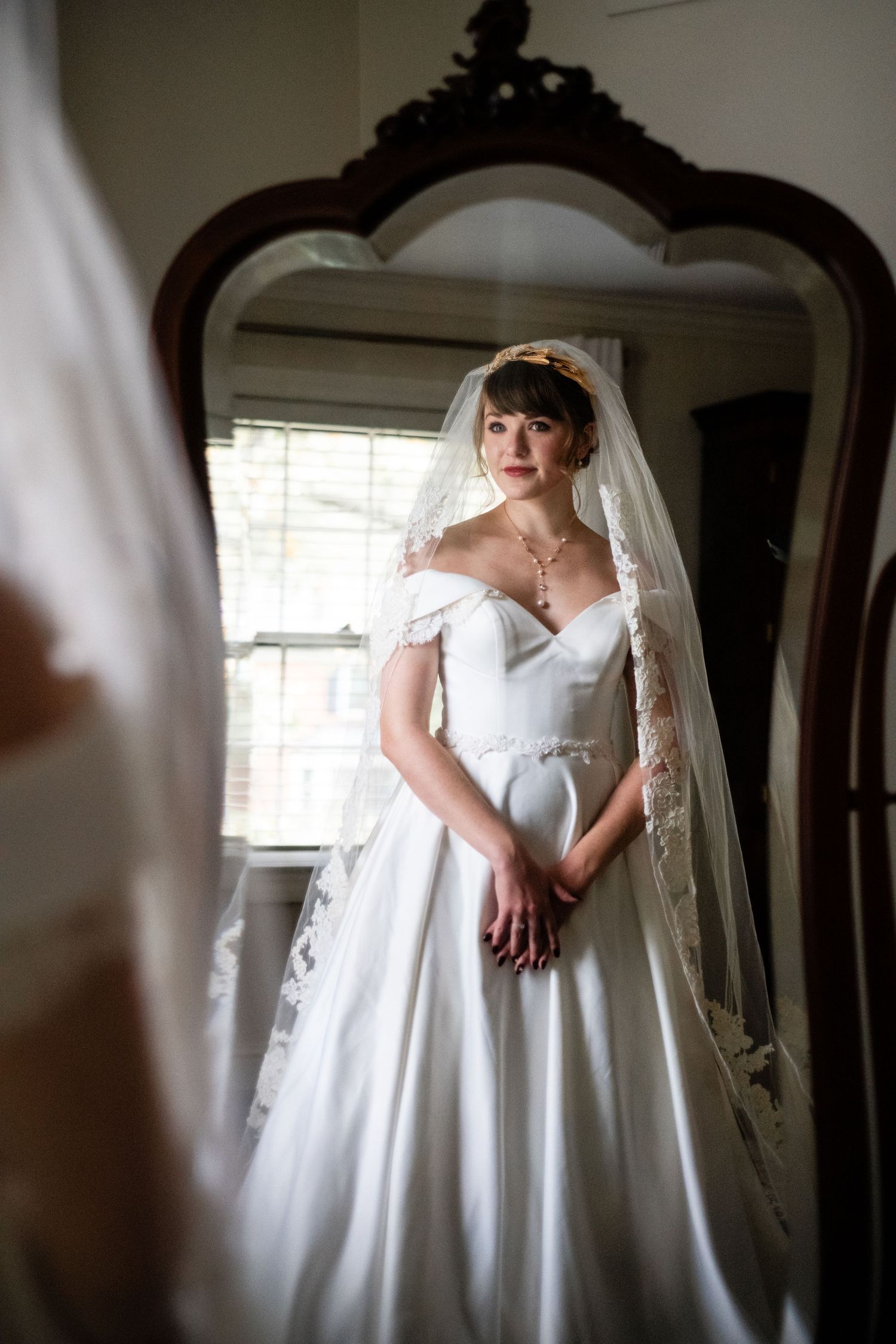 Elegant bridal portrait reflected in ornate vintage mirror with dramatic lighting.