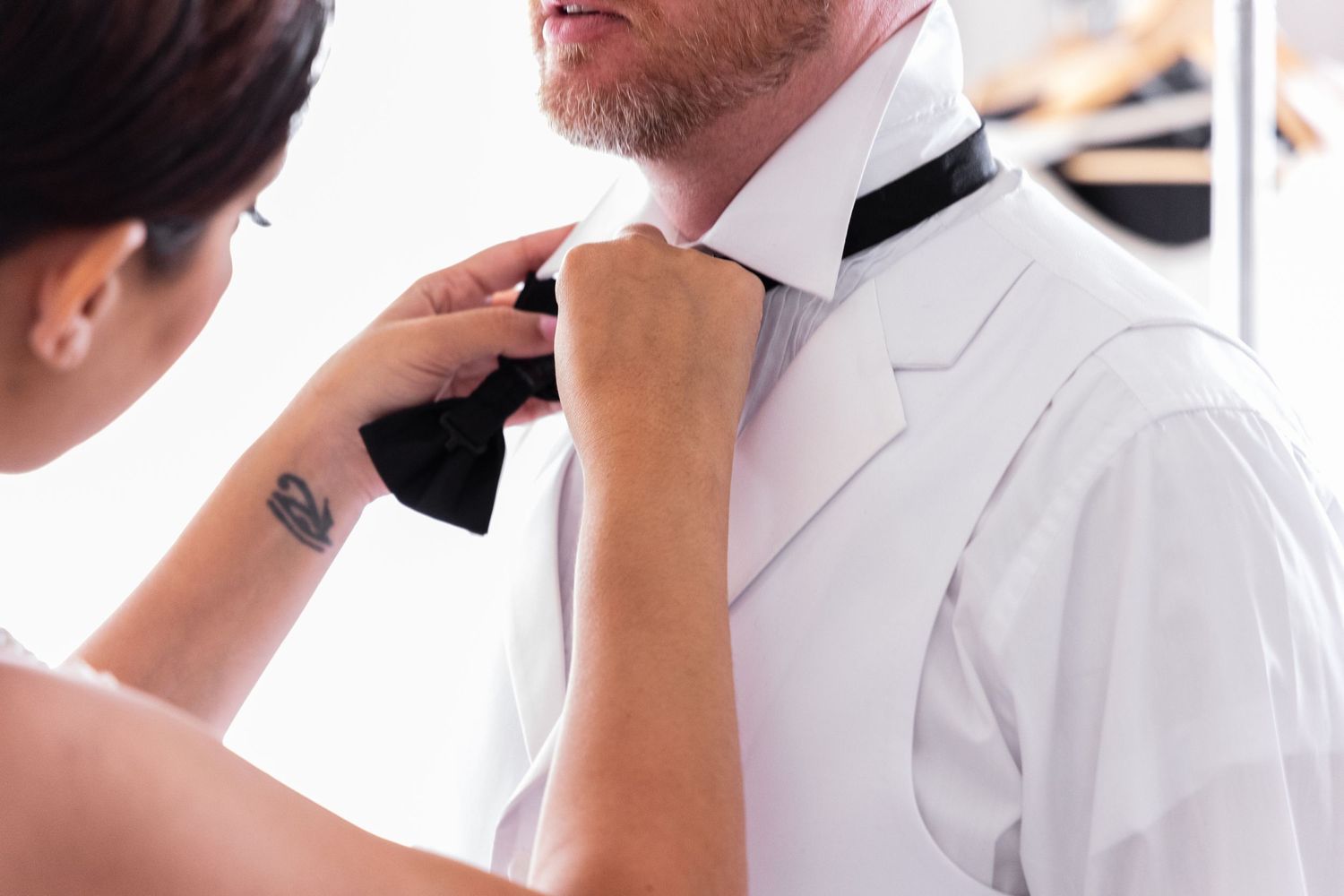 Close-up of hands adjusting black bow tie during wedding preparations.