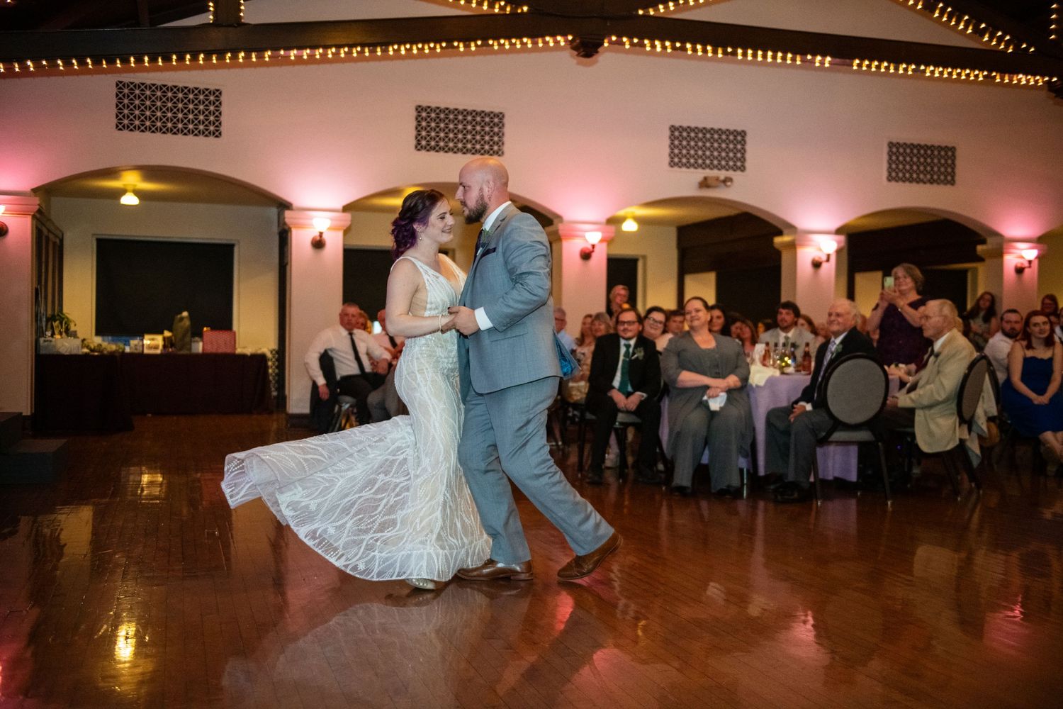 A couple performs their first dance in a beautifully lit reception hall.