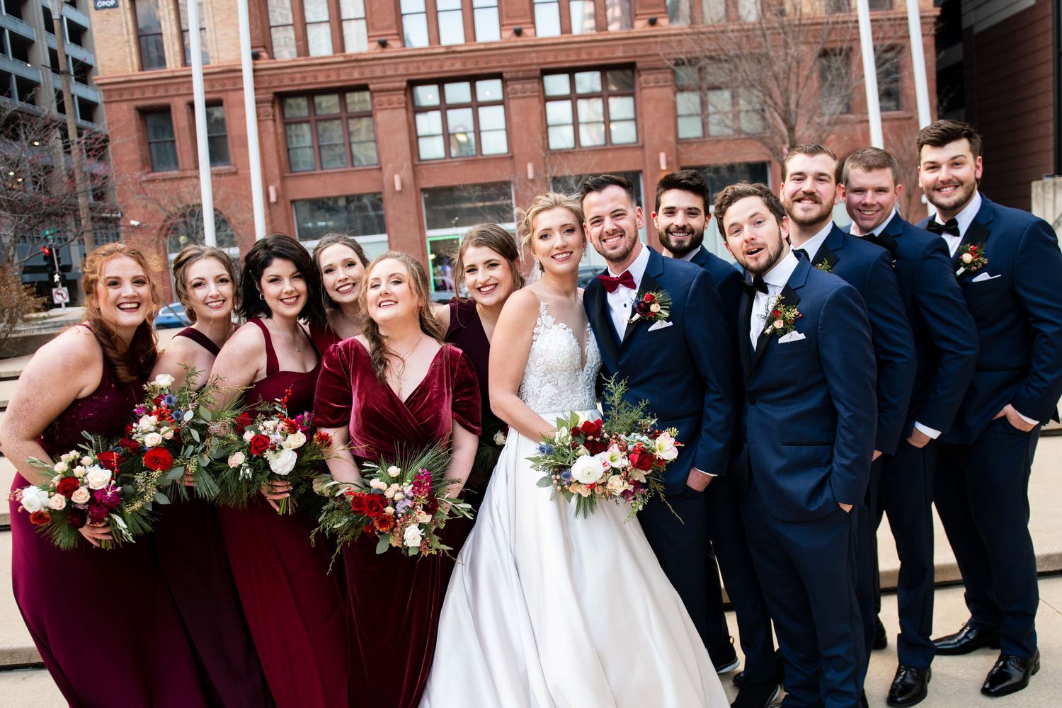 Wedding party in burgundy and navy attire poses outdoors with winter florals.