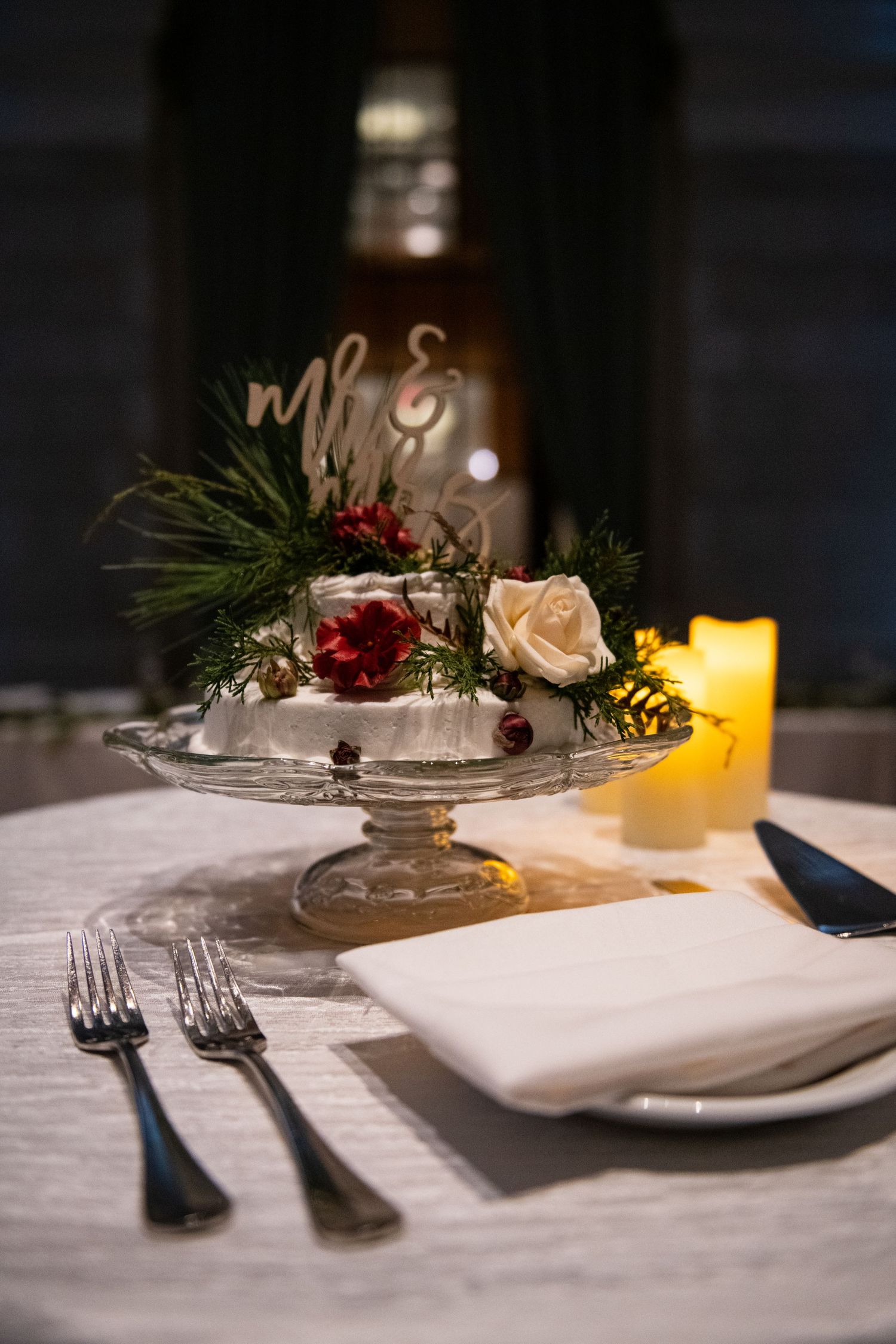Elegant place setting with rose centerpiece and candle at wedding reception.