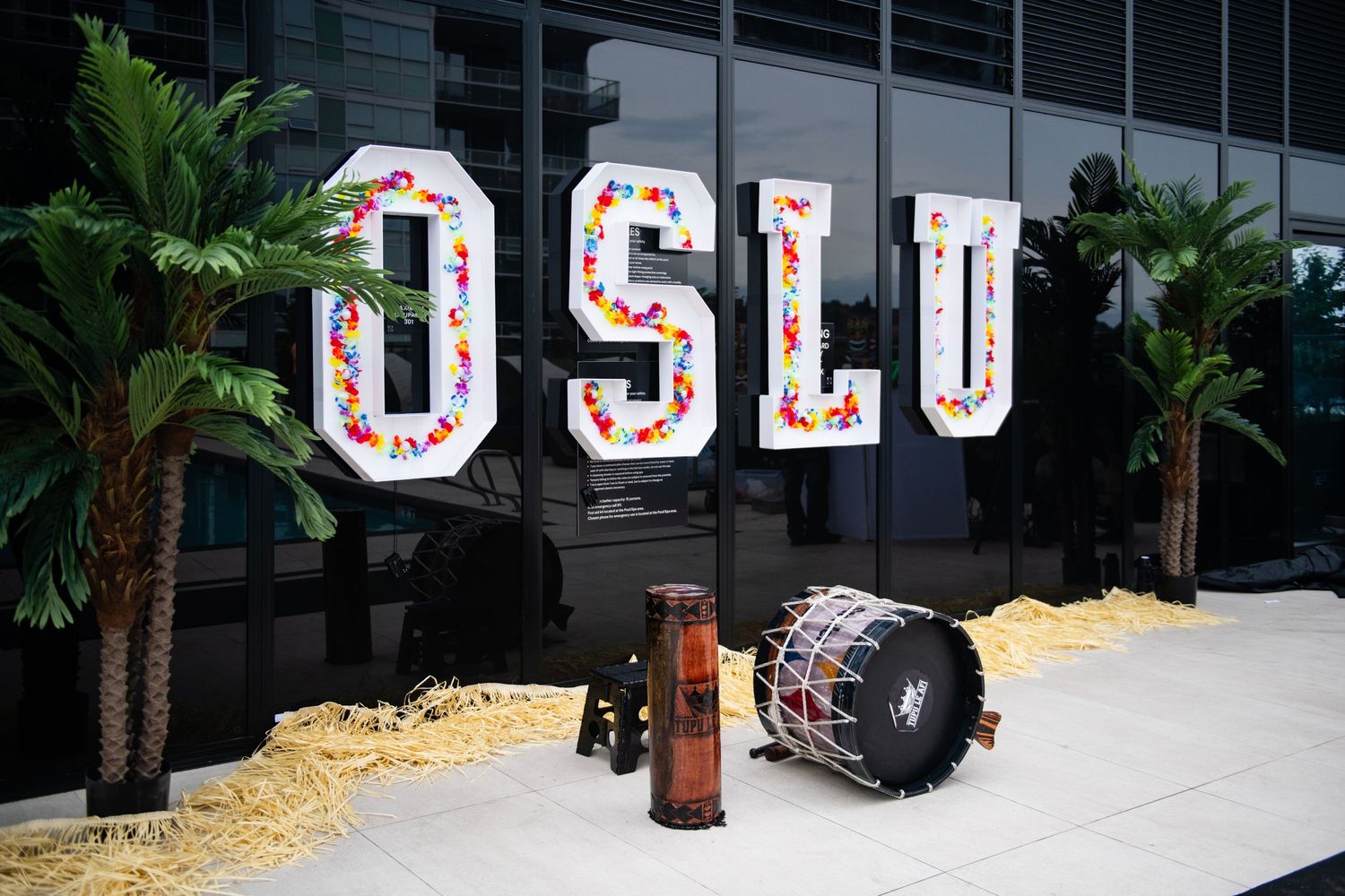 Large illuminated OSLU sign with decorative palm trees and props displayed outside building.