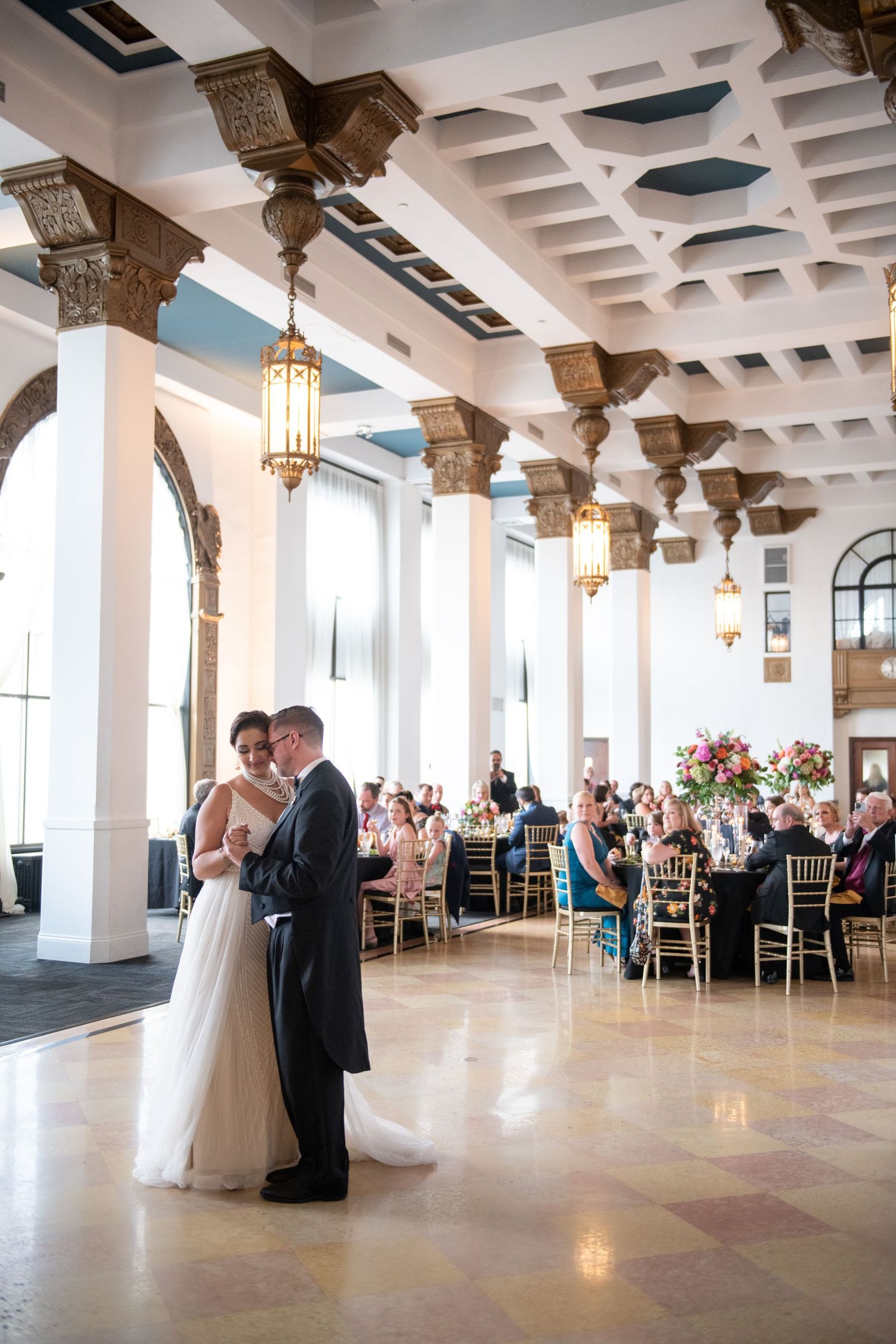 Elegant ballroom wedding reception with ornate columns and hanging lanterns during first dance.