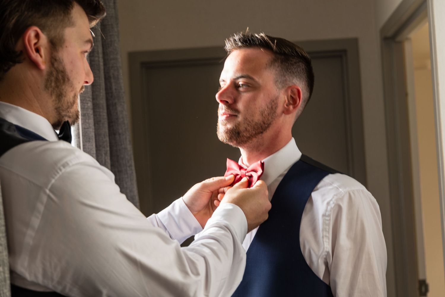 Best man helping the groom adjust his red bow tie before the wedding ceremony.
