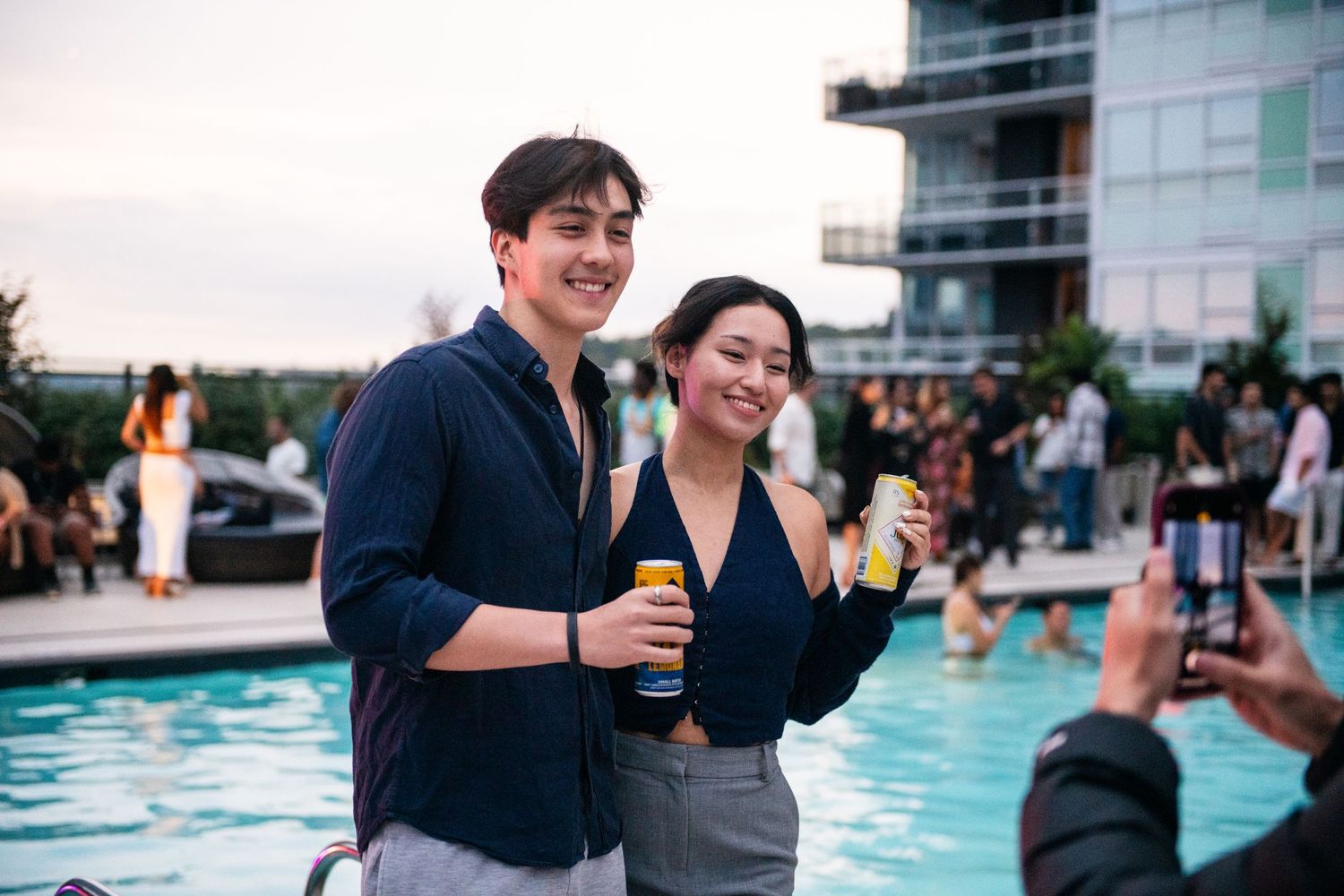Pair enjoying drinks at a poolside party during sunset.