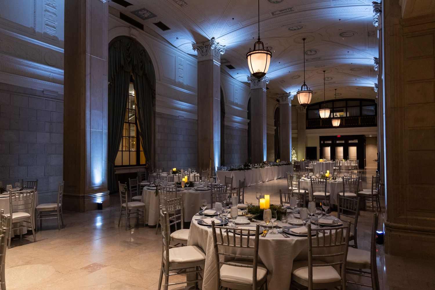 Classic ballroom interior with ornate columns, pendant lighting and formal table settings for an upscale event.