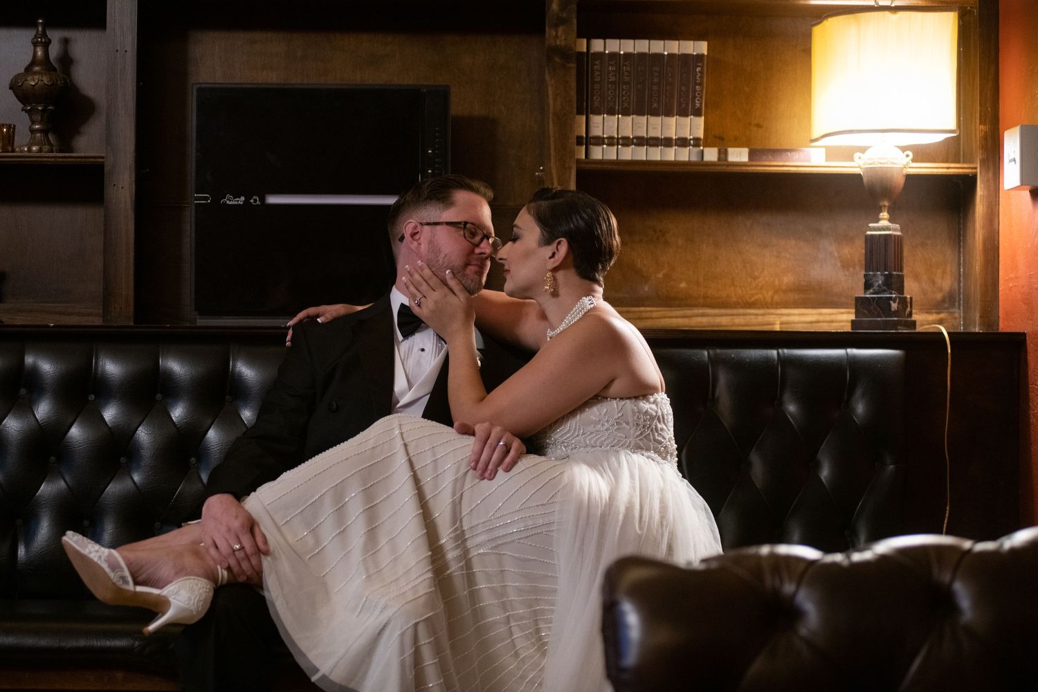A couple shares an intimate moment on a leather couch in warm lighting.